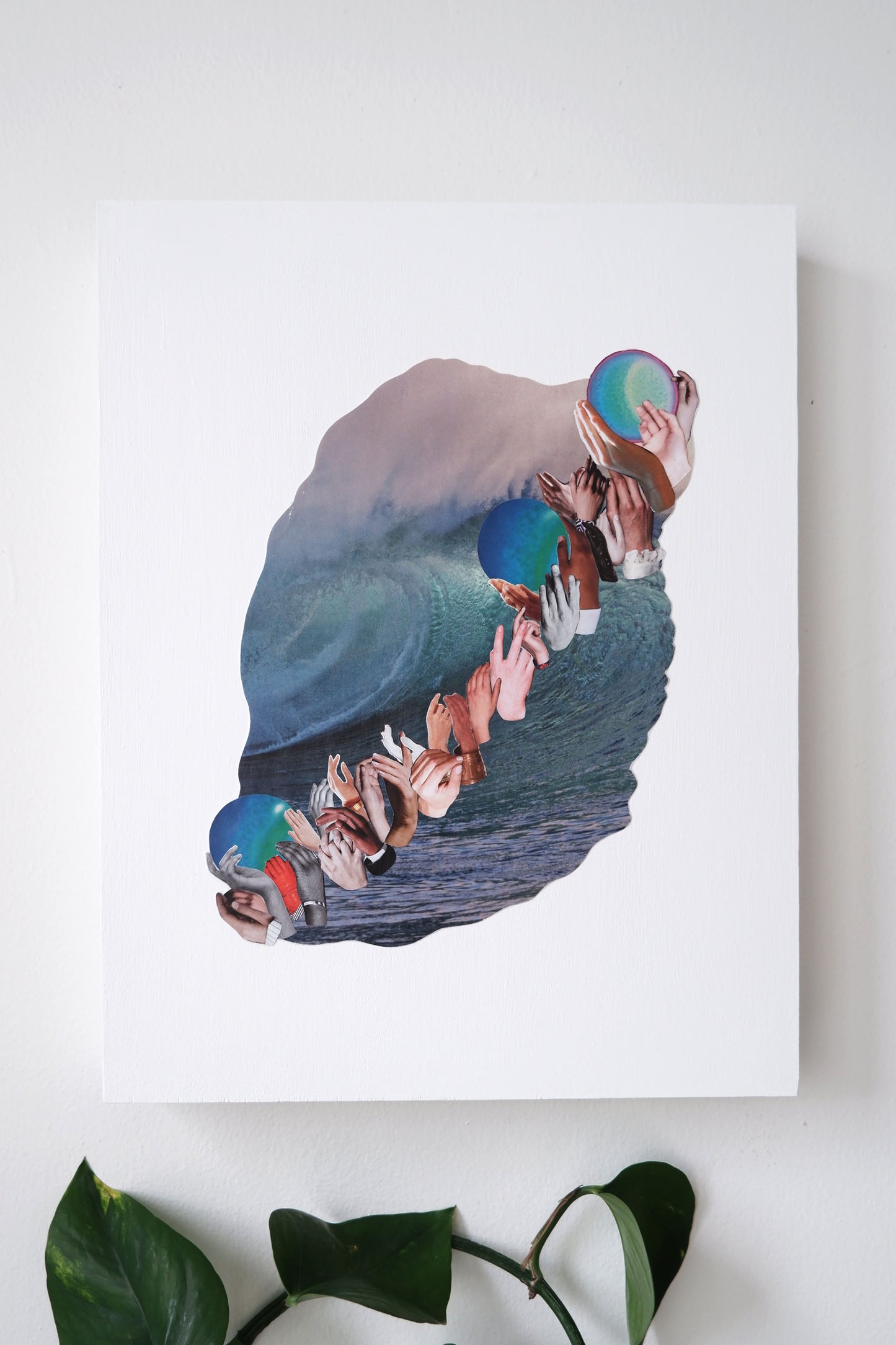 Original analog collage art "Three Waves" is a background image of a large rolling wave barrel with a white cap. A row of hands of diverse skin colour are layered and reaching diagonally up the ocean wave in a wave. the wave of hands moves images of the planet neptune up to the top.