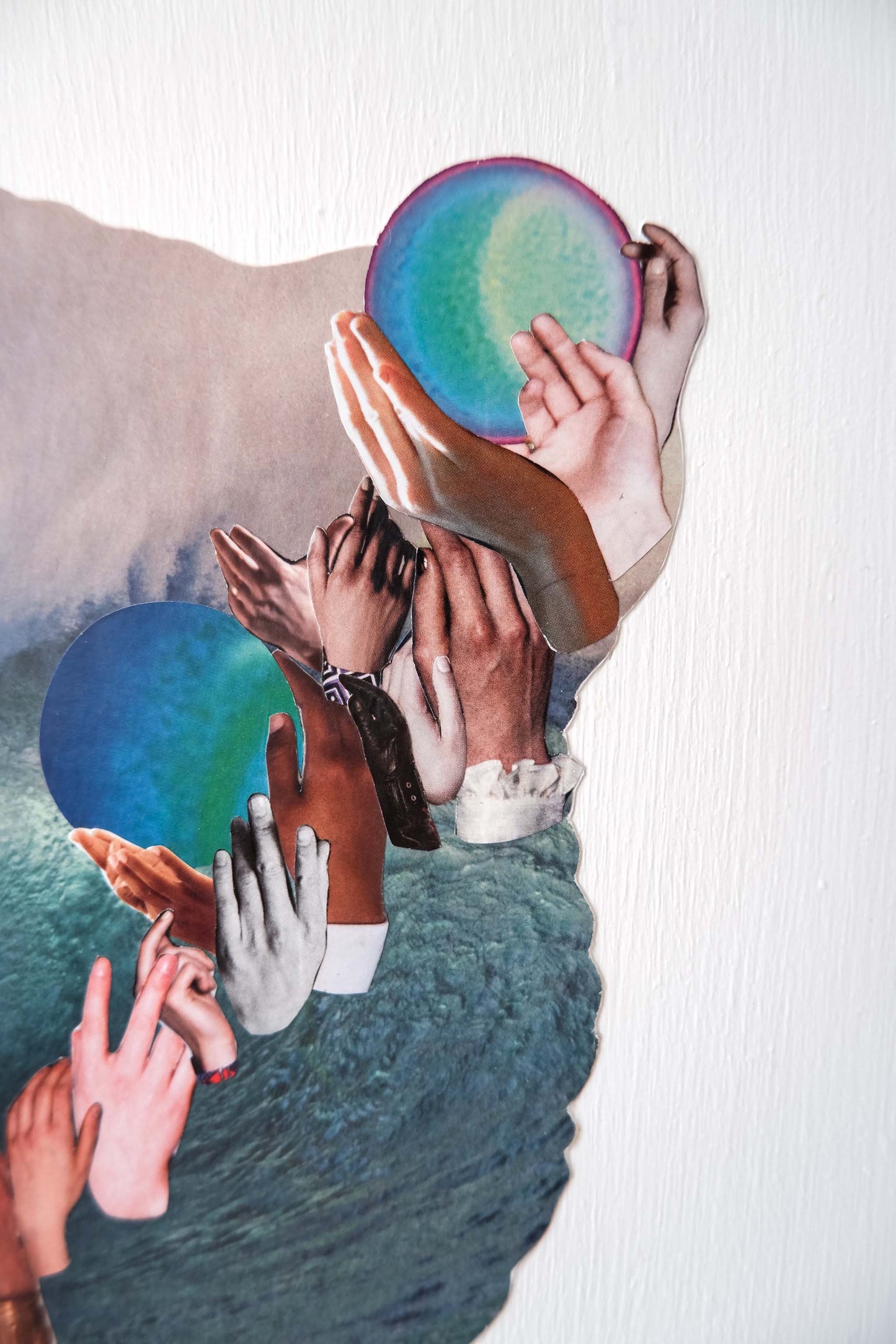 close up of Three Waves collage art, shows vertical paint texture of white background and details of images of diverse hands and neptune