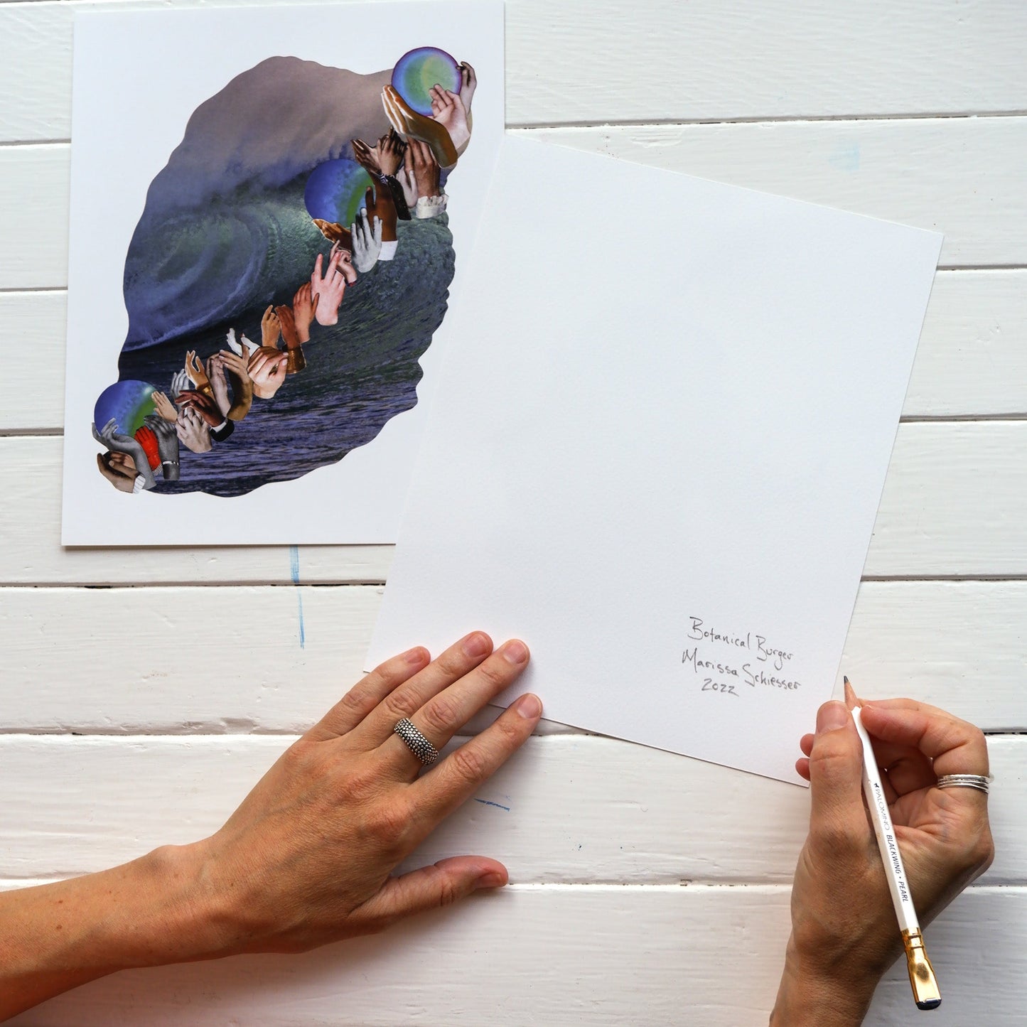 two hands signing the back of a fine art print on a table