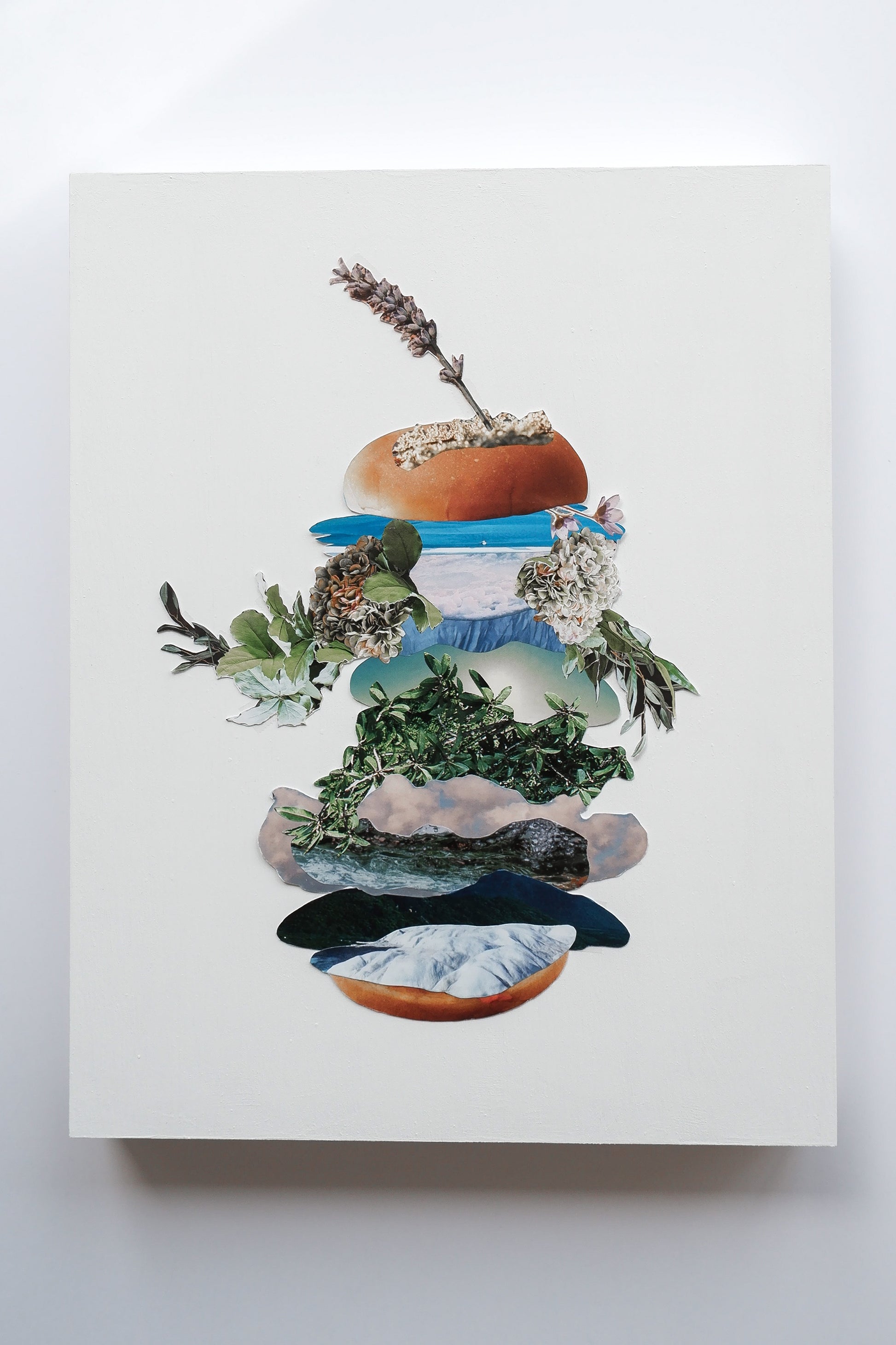 Original analog collage art of a tall "botanical burger" layered  images of plants, ocean, sky, clouds and flowers. A spear of lavender sticks out of the top bun.